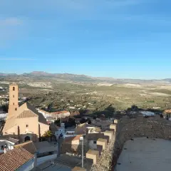 Vistas de Serón que ver: iglesia con campanario, tejados y paisaje rural montañoso bajo un cielo azul.