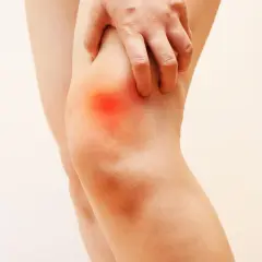 Mano che preme sul ginocchio con un'area rossa che indica dolore sopra al ginocchio.