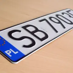Nowe tablice rejestracyjne z oznaczeniem PL i numerem SB 79035 leżą na drewnianym blacie.