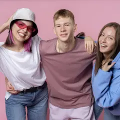 Trzech przyjaciół, pokolenie Z, uśmiecha się do aparatu na różowym tle.