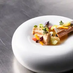 Delicato pesce in carpione, servito su un piatto bianco con verdure colorate e erbe aromatiche.