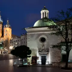 Nocny widok na Rynek Główny w Krakowie. W oddali majestatyczna Bazylika Mariacka, a na pierwszym planie kościół św. Wojciecha z zieloną kopułą.