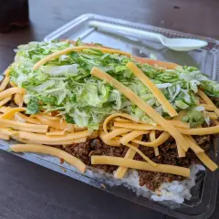 A hearty Okinawa taco rice dish, layered with white rice, seasoned ground meat, shredded lettuce, and melted cheese, ready to be enjoyed.