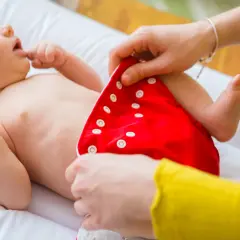 Mama zakłada dziecku czerwoną pieluchę tetrową. To pierwszy krok do tego, jak prać pieluchy tetrowe, by były czyste i ekologiczne.