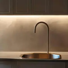 Rubinetto moderno su lavello in rame, con illuminazione a LED che valorizza la fascia di tamponamento cucina in resina spatolata.