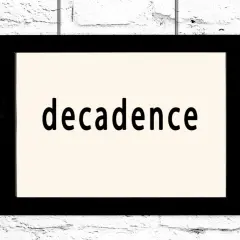 Czarno-biały obraz z napisem "decadence" na jasnym tle, wiszący na białej ceglanej ścianie. To pytanie: co to dekadentyzm?