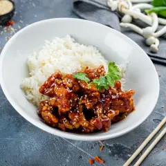 Pyszny kurczak bac bo w sosie z sezamem i ryżem, udekorowany kolendrą. Obok pałeczki i papryczki chili.