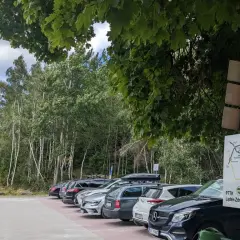 Samochody zaparkowane przy szlaku turystycznym na przełęczy kłodzkiej. W tle las i tablice informacyjne PTTK.