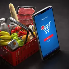 Koszyk z zakupami i smartfon z aplikacją do zamawiania jedzenia. M-commerce ułatwia zakupy spożywcze.
