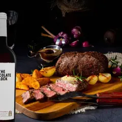 Zwei Flaschen Rotwein neben einem saftigen Wildbraten mit Beilagen. Perfekt, um die Frage zu beantworten: welcher rotwein zum wild kochen.