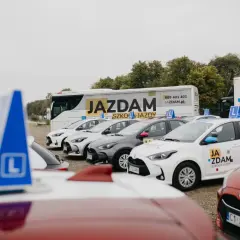 Samochody szkoleniowe z literą "L" i logiem "Ja Zdam" sugerują różne kategorie prawa jazdy.