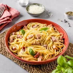 Un plato de carbonara italia, con espagueti, trozos de panceta, queso rallado y hojas de albahaca fresca.
