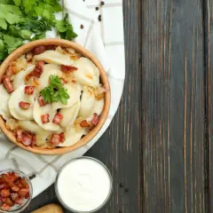 Pyszne pierogi z cebulką i skwarkami, serwowane w drewnianej misce. To klasyka kuchni łemkowskiej, podana z kwaśną śmietaną i świeżą natką pietruszki.