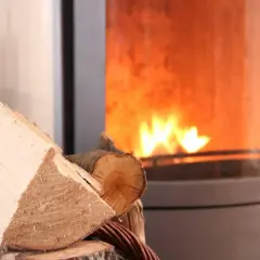 Holzscheite liegen bereit für den Kamin, der gerade nicht benutzt wird. Ein Schornsteinfeger würde sich über die Sauberkeit freuen.