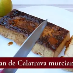 Un cuchillo corta un trozo de pan de Calatrava murciano, un postre dulce y dorado, servido en un plato blanco.