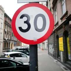 Znak ograniczenia prędkości do 30 km/h. Czy skrzyżowanie odwołuje ograniczenie prędkości? Ulica z samochodami i kamienicami.