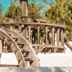 El pozo de los frailes que ver: una noria de madera antigua, rodeada de vegetación exuberante y bajo un cielo azul brillante.