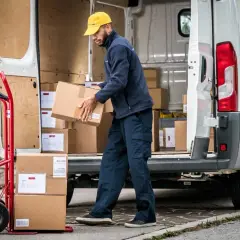 Zusteller lädt Pakete aus einem Lieferwagen. Viele Pakete, vielleicht wegen des peak season surcharge.