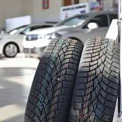 Dwa nowe opony Lassa z kolorowymi paskami, gotowe do montażu na samochodach w tle.