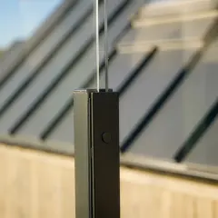 Detaljbild av ett fäste för att montera vindskydd. Glaspanelen är infälld i en svart stolpe.