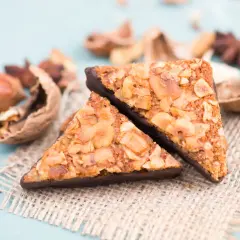 Zwei dreieckige Nussecken mit Schokoladenboden, umgeben von verschiedenen Nüssen und Gewürzen. Ein köstliches nussecken rezept.
