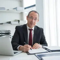 Mężczyzna w garniturze podpisuje umowę najmu u notariusza. Na biurku laptop i dokumenty.