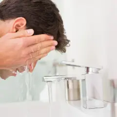 Mann wäscht sein Gesicht mit kaltem Wasser. Er hält seine Hände unter den Wasserhahn, um das Gesicht zu erfrischen.