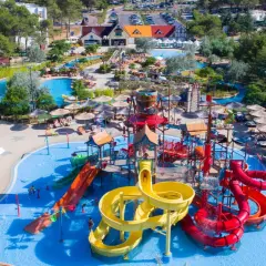 Un camping pour camping-car avec parc aquatique, offrant toboggans colorés, piscines et parasols pour des vacances en famille sous le soleil.