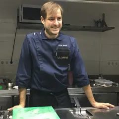 Javier Muñoz chef sonríe en la cocina, con su uniforme azul y el logo de "La Carbona".