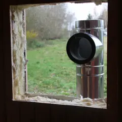 Przejście komina przez ścianę drewnianą, z widocznym izolacyjnym materiałem.
