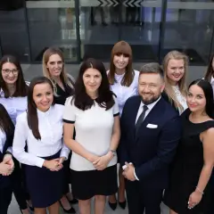 Grupa prawników i radców prawnych w garniturach i eleganckich strojach stoi przed budynkiem.