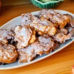 Leckere Apfelkrapfen in der Pfanne, goldbraun gebacken und mit Zuckerguss überzogen, liegen auf einem Teller.