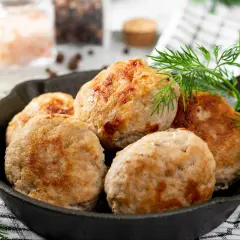 Pięć dietetycznych kotletów mielonych z indyka z piekarnika, podanych w żeliwnej patelni, ozdobione gałązką koperku.