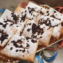 Chiacchiere morbide cosparse di zucchero a velo e gocce di cioccolato, pronte per festeggiare il Carnevale.