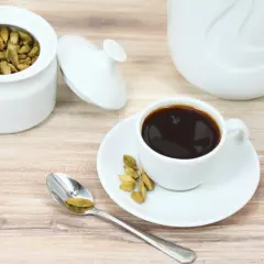 Biały dzbanek, cukiernica z kardamonem do kawy i filiżanka czarnego napoju na drewnianym blacie.
