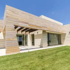 Moderna finca en Madrid con fachada de piedra y madera, césped verde y cielo azul.