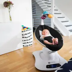 Sover gott i sin mamaroo babysitter. En bebis vilar i en svart gunga med leksaker ovanför.