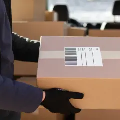 Kurier DPD z paczką w rękach, gotowy do dostarczenia. Na kartonie widoczny list przewozowy.