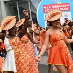 Des danseuses en tenues orange et blanches, chapeaux assortis, célèbrent la foire de Paris 2026 dans une ambiance festive.