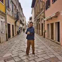 Mann steht in einer Gasse mit Kopfsteinpflaster in Poreč. Ein Eisgeschäft und Boutiquen säumen die Straße. Ein toller Ort für Poreč Geheimtipps.