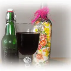 Szklanka z ciemnym winem z wiśni obok zielonej butelki i ozdobionej kwiatami butelki z różową kokardką.