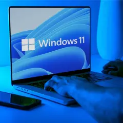 Ręce na klawiaturze laptopa z logo Windows 11. Dowiedz się, jak wejść do BIOS-u w Windows 11.