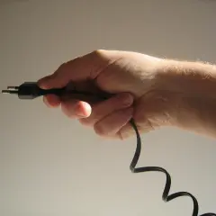 Dłoń trzymająca czarny kabel z wtyczką.