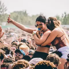 Menschen feiern ausgelassen beim **pulse open air**. Eine Frau hält ihr Handy hoch, während eine Freundin sie umarmt.