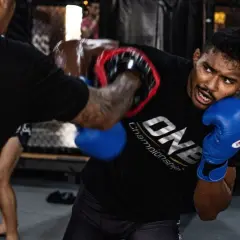 Fighter in blue gloves dodges an overhand punch during intense MMA training.