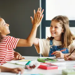 Kinder geben sich High-Five, während sie konzentriert arbeiten. Dieses Bild zeigt eigenverantwortliches Arbeiten und Freude am Lernen.
