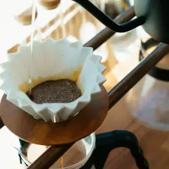 Delikatny strumień wody zaparza kawę po japońsku w papierowym filtrze.