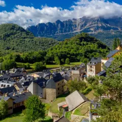 Pueblos del Pirineo Catalán, con tejados oscuros y montañas verdes de fondo bajo un cielo azul con nubes.