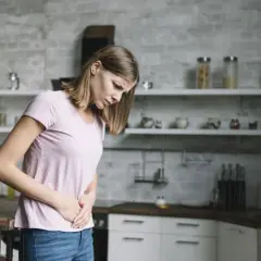 Kobieta w kuchni trzyma się za brzuch, odczuwając ból. Może to być jeden z objawów chlamydii.