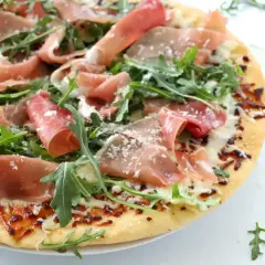 Pyszna pizza prosciutto z rukolą i parmezanem, idealna na letni wieczór.